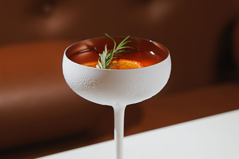 A cocktail with rosemary and oranges garnish on a table at Prego Italian Restaurant at The Westin Resort Nusa Dua