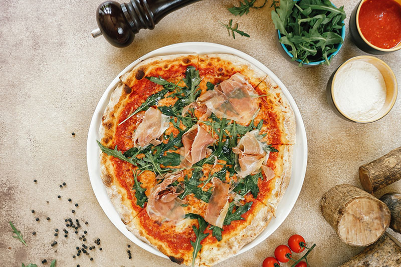 Pizza with ruccola and ham toppings on a plate at Prego Italian Restaurant at The Westin Resort Nusa Dua