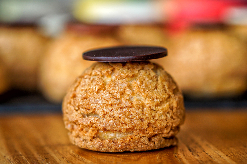 A golden cream puff topped with a dark chocolate disc at Poule de Luxe Bali