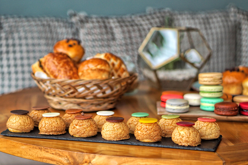 Elegant display of colorful macarons, cream puffs and freshly baked pastries on a wooden table at Poule de Luxe Bali