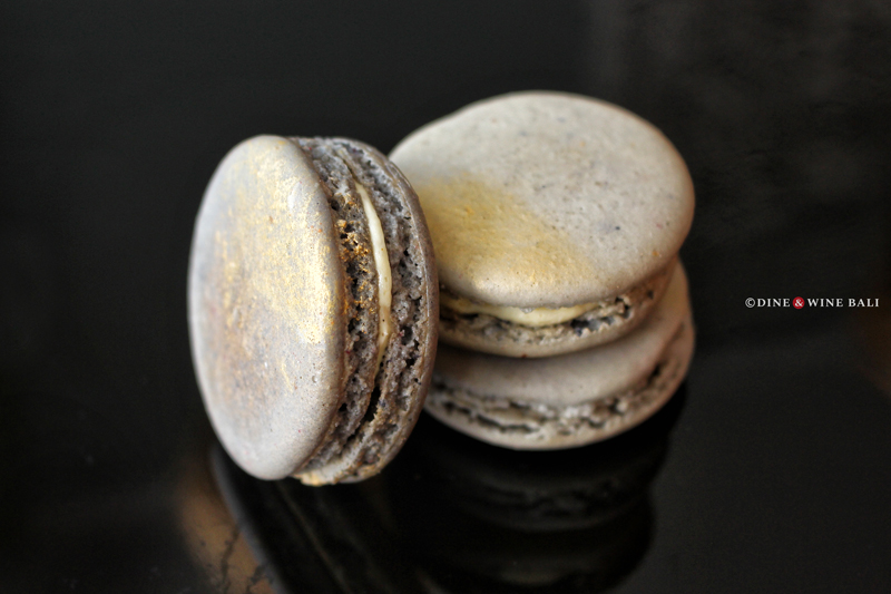 Elegant gray macarons with a gold shimmer, stacked on a sleek black surface at Poule de Luxe Bali