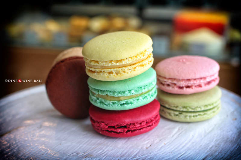 Colorful macarons stacked on a white surface, featuring vibrant shades of yellow, green, red, pink, and chocolate brown at Poule de Luxe Bali