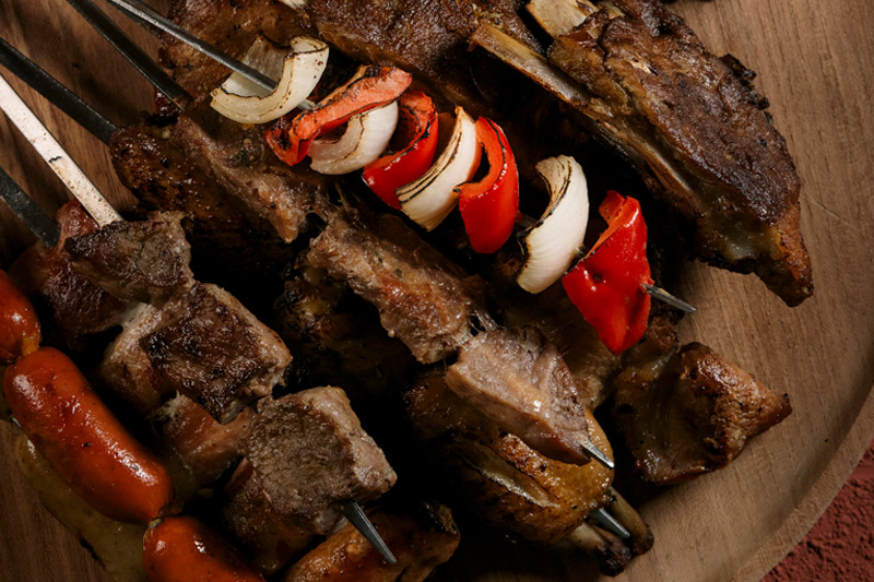 A Brazilian BBQ platter featuring skewered meats, grilled sausages, roasted vegetables, and dipping sauces on a wooden plate at Valle Canggu Padang Linjong